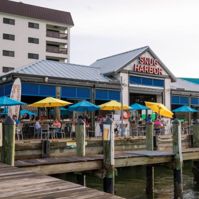 snug harbor waterfront restaurant with blue and yellow outdoor umbrellas and pier in view